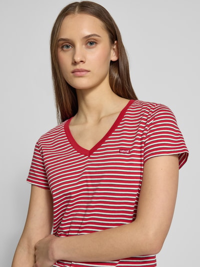 Modelka kobieca ma na sobie T-Shirt mit V-Ausschnitt und Label-Stitching od Levi's®, bawełna, krój regular fit, czerwono-białe paski, zbliżenie na górną część ciała. Długość tyłu w rozmiarze S: 58 cm.