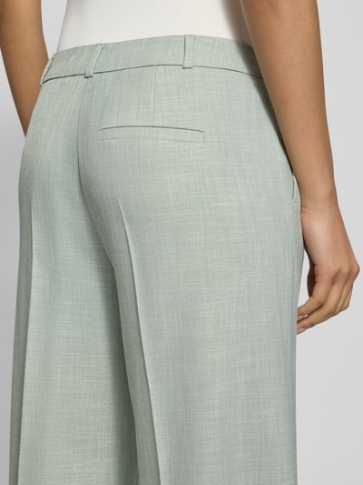 Vrouwenmodel draagt Wide Fit Stoffhose aus Viskose-Mix mit Bügelfalten van comma, lichtgroen, elastische viscosemix, achterzakken, haak- en ritssluiting, detailopname rug.