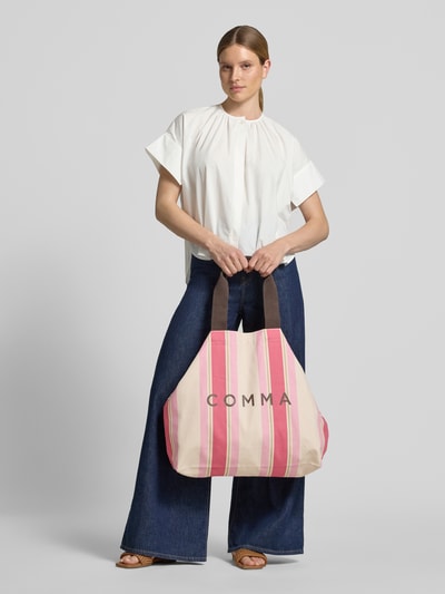 Frauenmodel trägt Tote Bag mit Logo-Print von comma aus reiner Baumwolle, rosa Streifen, offenes Hauptfach, Ganzkörperansicht von vorne.
