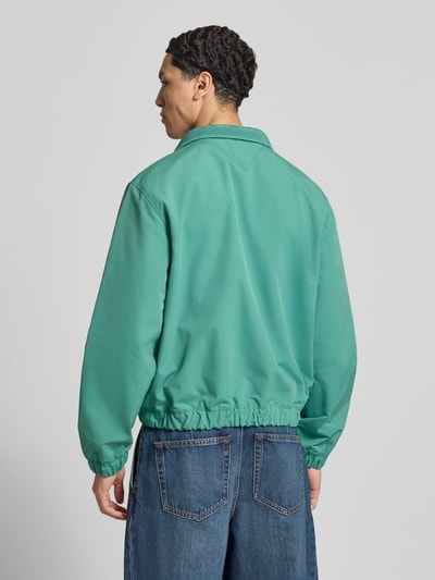 Männermodel trägt Regular Fit Blouson von Tommy Jeans, unifarben, Stehkragen, elastische Bündchen, seitliche Taschen, Ganzkörperansicht Rückansicht.