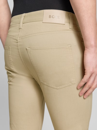 Männermodel trägt Slim Fit Modell Chino aus Baumwoll-Mix 'DELAWARE5' von BOSS in Beige mit Label Patch, Detailaufnahme Rückansicht.