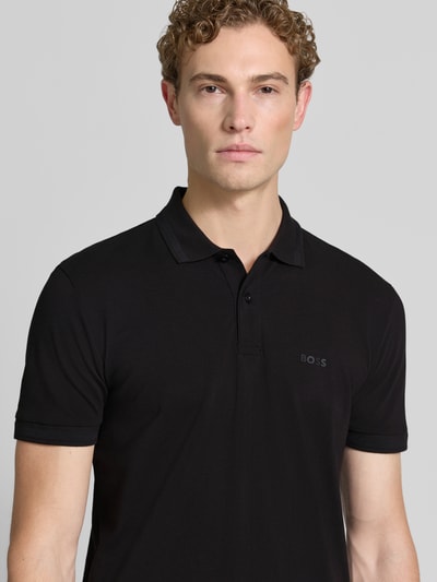 Männermodel trägt schwarzes Regular-Fit Poloshirt aus reiner Baumwolle Modell 'PIO 1' von BOSS Green, Nahaufnahme Oberkörper.