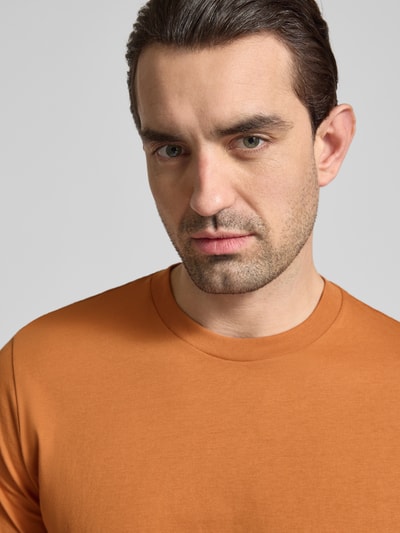 Mężczyzna nosi T-Shirt mit Rundhalsausschnitt von Schiesser, bawełniany materiał w kolorze ceglastym, krój regular fit, zbliżenie na górną część ciała