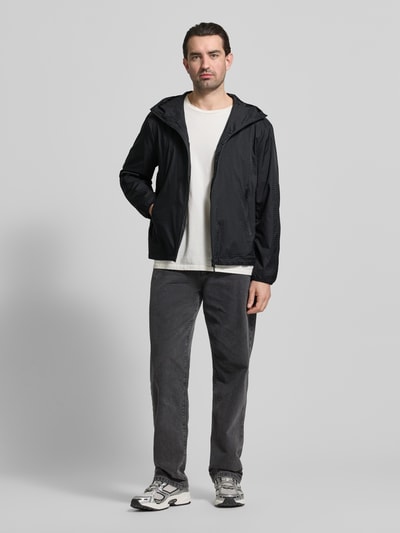 Männermodel trägt Jacke mit Zweiwege-Reißverschluss von Emporio Armani in Schwarz, kombiniert mit grauer Hose, Ganzkörperansicht von vorne. Regular Fit mit Kapuze und Reißverschlusstaschen.