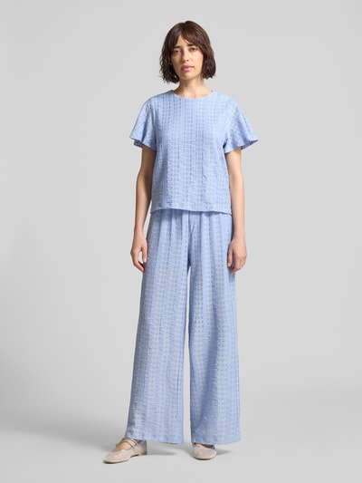 Kobiece modelka nosi Kurzarmbluse mit Lochstickerei Modell 'CASSANDRA' od Vero Moda, jasnoniebieska, jednolity kolor, krój regular fit, okrągły dekolt, krótki rękaw, ażurowa struktura materiału, widok całej sylwetki z przodu.