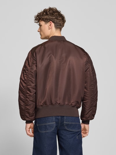 Männermodel trägt Regular Fit bomberjack met opstaande kraag model 'Heritage' van Alpha Industries, ruglengte maat M 63 cm, klepzak, ritssluiting, elastische boorden, schouderbreedte maat M 50 cm, borstwijdte maat M 57 cm, gladde textuur, donkerbruin, Ganzkörperansicht Rückansicht.