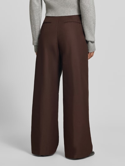 Frauenmodel trägt Relaxed Fit Stoffhose aus Baumwoll-Mix von MYON in Dunkelbraun, glatte Textur, breite Kellerfalten, Ganzkörperansicht Rückansicht.