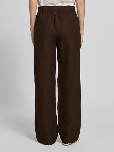 Männermodel trägt Regular Fit Weite Hose aus reinem Leinen Modell 'FARINA' von Brax, brązowy kolor, gładki materiał, elastyczny pas z tunelem, kieszenie boczne, krój regular fit, widok całej sylwetki z tyłu.