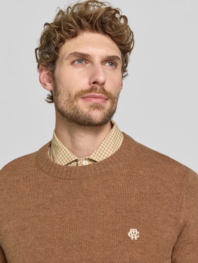 Männermodel trägt Slim Fit Strickpullover aus reiner Wolle mit Label-Stitching von MCNEAL, braun, gerippte Abschlüsse, Nahaufnahme Oberkörper.