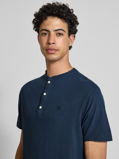 Männermodel trägt T-Shirt mit kurzer Knopfleiste von Superdry in Dunkelblau, Baumwoll-Mix mit Leinen-Anteil, Nahaufnahme Oberkörper.