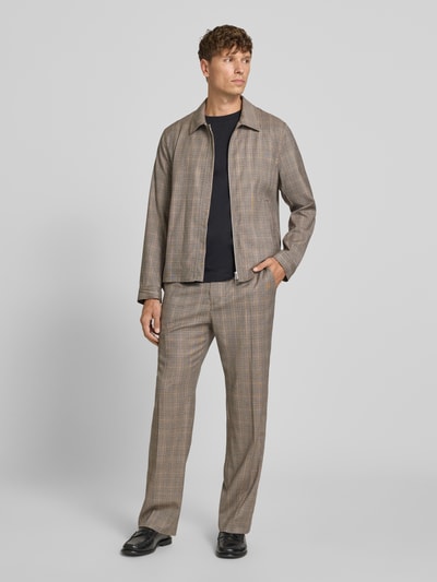 Męski model nosi spodnie materiałowe Straight Fit Stoffhose mit Bügelfalten Modell 'Cove' von Tiger Of Sweden, beżowo-brązowa kratka, czarne buty, czarna koszulka, szerokość w rozmiarze 50: 39 cm, długość wewnętrzna nogawki: 80 cm, bawełna, wpuszczane i kieszenie z tyłu, elastyczny pas z tunelem, całopostaciowy widok z przodu.