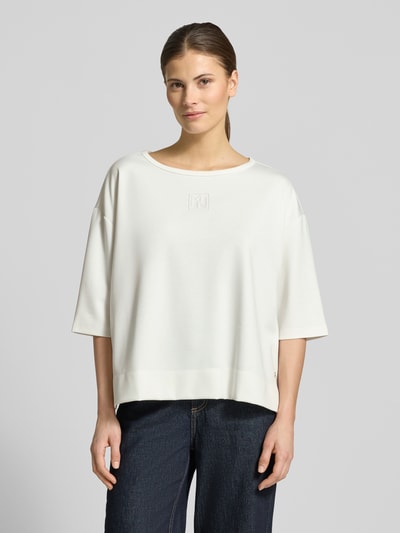 Frauenmodel trägt T-Shirt mit Rundhalsausschnitt und Logo von monari, Damen T-Shirt im Relaxed-Fit Material-Mix mit Viskose-Anteil, helle Farbe, glatte Textur, Ganzkörperansicht von vorne.