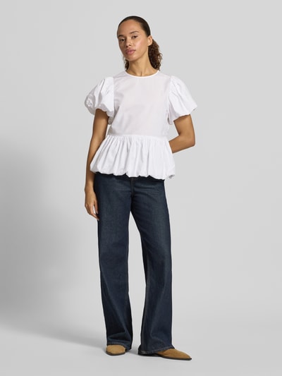 Modelka nosi Blusenshirt mit Puffärmeln von Copenhagen Muse, biała bawełna, krój slim fit, okrągły dekolt, bufiaste rękawy, marszczenia, zamek z tyłu, długość tyłu S: 58 cm, długość rękawa S: 18 cm, ciemnoniebieskie spodnie, kwadratowe formy, gładka tekstura, widok całej sylwetki z przodu.