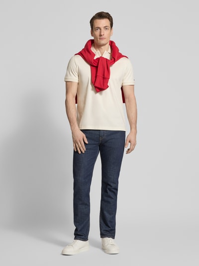 Männermodel trägt Regular Fit Poloshirt aus reiner Baumwolle von Tommy Hilfiger in Unifarbe, Logo-Detail, Ganzkörperansicht von vorne.