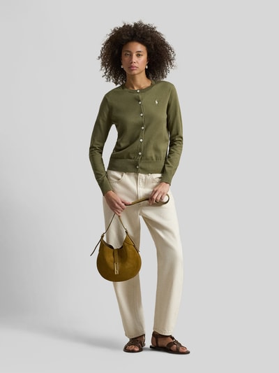 Frauenmodel trägt Regular Fit Strickjacke mit Logo-Stitching von Polo Ralph Lauren in Olivgrün, Rundhalsausschnitt, cremefarbene Hose, Ganzkörperansicht von vorne.