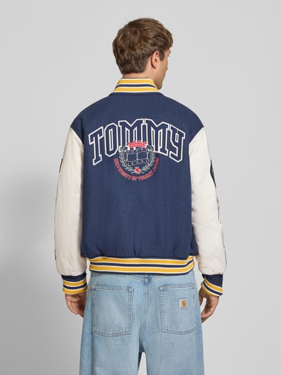 Männermodel trägt Regular Fit Bomberjacke aus Woll-Mix Modell 'LETTERMAN' von Tommy Jeans in Blau und Weiß, breite gelbe Bündchen, Ganzkörperansicht Rückansicht, Herren Bomberjacke / Blouson.