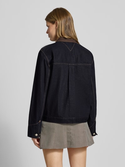 Frauenmodel trägt Oversized Jeansjacke aus reiner Baumwolle von Tommy Jeans in dunklem Blau, Denim-Struktur, Rückenpasse mit Falte, Ganzkörperansicht Rückansicht.