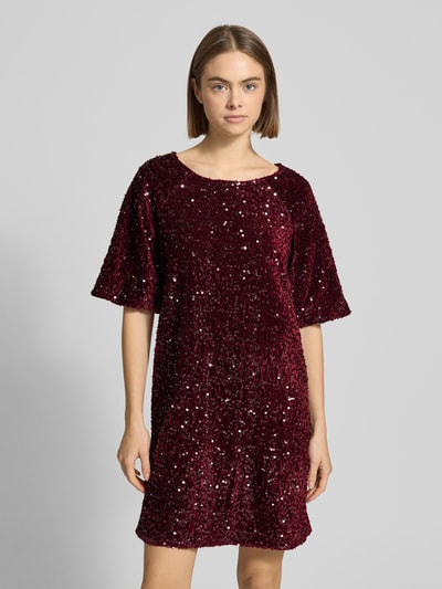 Kobiece model prezentuje sukienkę koktajlową z cekinowym obszyciem 'Schmales Cocktailkleid mit Paillettenbesatz Modell 'KAM' von Pieces', efekt: jednolity kolor, błyszczący, krój: wąski, długość mini, dekolt w łódkę, wyhaftowane logo, materiał: aksamit, krótki rękaw, prosty dół, aksamitna powierzchnia, kolor bordowy, całkowity widok z przodu.