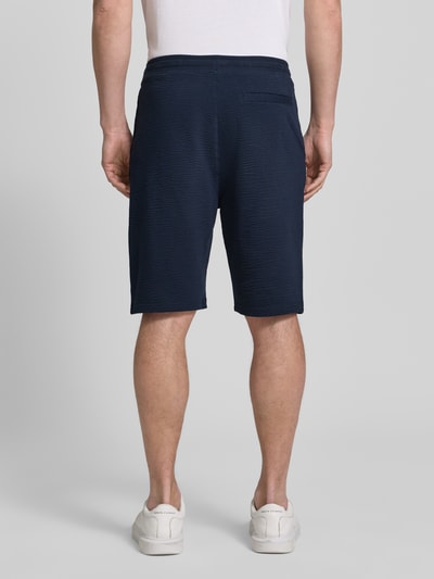 Mężczyzna nosi Relaxed Fit Bermudas aus Baumwoll-Mix Modell 'DETROIT' od s.Oliver RED LABEL, granatowy, faktura waflowa, widok całej sylwetki od tyłu.