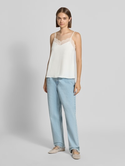 Kobieta nosi białą bluzkę o luźnym kroju z obszyciem koronką model 'TIFFANY' od PIECES, jasnoniebieskie spodnie, jednolite kolory, pełen widok z przodu.