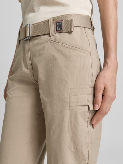 Frauenmodel trägt Bermudas mit Pattentaschen und Saum mit fixiertem Aufschlag von G.I.G.A. DX in Beige, Struktur leicht glänzend, seitliche Eingrifftaschen, Knopf- und Reißverschluss, Gürtel, Label-Patch, Detailaufnahme seitlicher Oberschenkel.