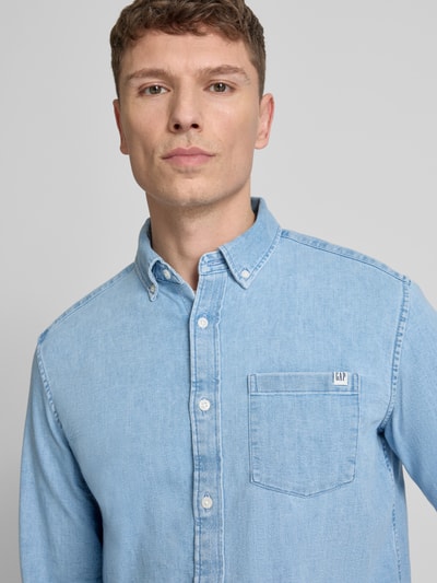 Mannenmodel draagt Regular Fit Jeanshemd met Button-Down-Kraag van GAP, lichtblauw, borstzak, labeldetail, katoenmix met stretch, close-up bovenlichaam.