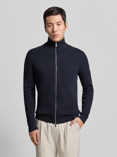 Männermodel trägt Regular Fit Strickjacke aus reiner Baumwolle Modell 'DAME' von SELECTED HOMME, dunkelblau, Zweiwege-Reißverschluss, unifarben, Stehkragen, Strickstruktur, ganzkörperansicht von vorne.