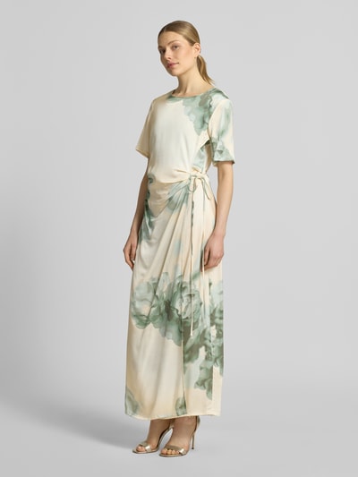 Frauenmodel trägt Maxikleid in Wickel-Optik mit Schnürung Modell 'Kylar' von mbyM aus Reine Viskose, florale Muster, Taillierter Schnitt, Rundhalsausschnitt, sanfte Grüntöne auf cremefarbenem Stoff, Ganzkörperansicht von vorne.