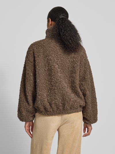 Frauenmodel trägt Jacke mit Stehkragen von JAKE*S STUDIO WOMAN o luźnym kroju, stójka, zamek błyskawiczny, wpuszczane kieszenie, elastyczne zakończenia rękawów, długość tyłu 60 cm, szerokość ramion 58 cm, szerokość klatki piersiowej 65 cm, długość rękawów 56 cm, brązowa faktura baranka, widok całej sylwetki z tyłu.
