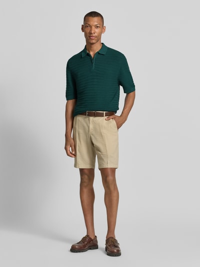 Männermodel trägt Regular Fit Poloshirt mit kurzem Reißverschluss von MCNEAL, Baumwoll-Mix mit Viskose-Anteil, Strukturmuster, Polokragen, sandfarbene Shorts, grüner Farbton, glatte Textur, Ganzkörperansicht von vorne.
