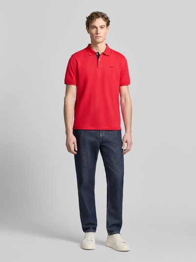 Männermodel trägt Regular Fit Poloshirt mit Logo-Stitching von Gant in Rot, elastischer Baumwoll-Mix, Ganzkörperansicht von vorne.