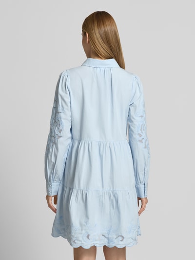 Frauenmodel trägt knielanges Hemdblusenkleid mit Lochstickerei Modell 'Zimia' von YAS aus reiner Baumwolle, taillierte Passform, langärmelig, Umlegekragen, durchgehende Knopfleiste, hellblau, florale Details, Textur durch zarte Lochstickerei, Rückenlänge bei Größe 36: 92 cm, Brustweite 51 cm, Ärmellänge 67 cm, Ganzkörperansicht Rückansicht.