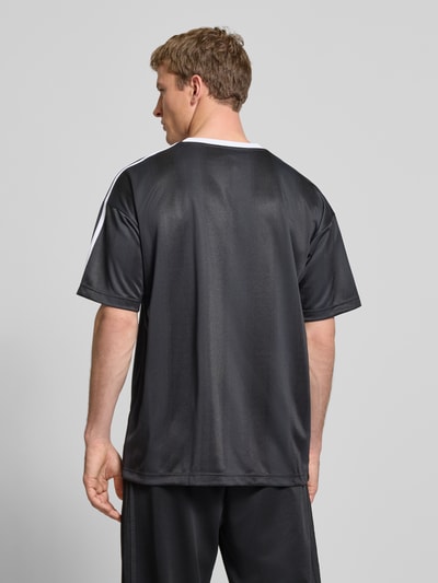 Männermodel trägt Funktionsshirt mit Logo und Rundhalsausschnitt von adidas Originals, schwarz mit weißen Kontraststreifen, Regular Fit, Rückenlänge 75 cm, Ganzkörperansicht Rückansicht.