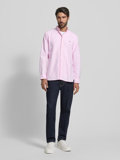 Männermodel trägt Regular Fit Freizeithemd aus reiner Baumwolle von Tommy Hilfiger in zartem Rosa, Allover-Muster, Unifarben, Regular-Fit, einreihige Knopfleiste, Button-Down-Kragen, Applikation: Label-Detail, Rückenpasse mit Kellerfalte, Langarm, leicht abgerundeter Rumpfabschluss, Material: reine Baumwolle, Ganzkörperansicht von vorne.
