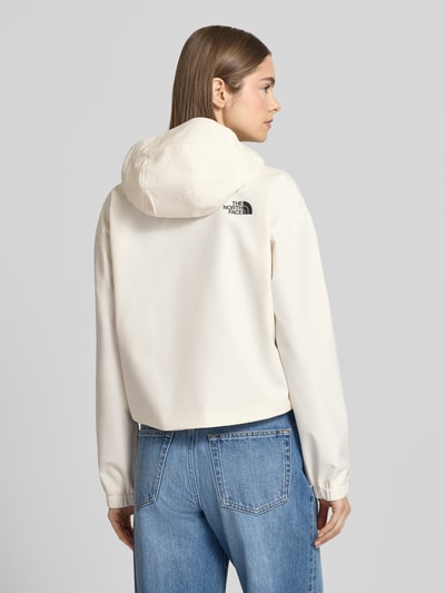 Młody modelka nosi Cropped Jacke mit Logo und Reißverschluss von The North Face, kremowa, kaptur, logo, suwak, jeansy, całkowity widok z tyłu. Długość tyłu w rozmiarze S: 58 cm, szerokość ramion w rozmiarze S: 54 cm, szerokość klatki piersiowej w rozmiarze S: 50 cm, długość rękawa w rozmiarze S: 56 cm.