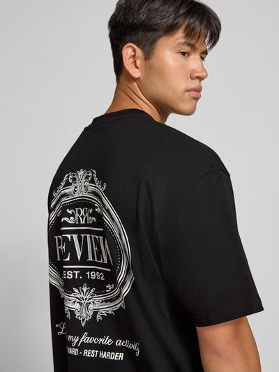 Männermodel trägt schwarzes Regular Fit T-Shirt aus reiner Baumwolle mit weißem rückseitigem Print von REVIEW, Nahaufnahme Rückansicht.