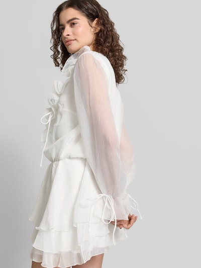 Vrouwenmodel draagt Minikleid met Rüschen und V-Ausschnitt van Gina Tricot in wit, getailleerd model, mouwen met vetersluiting, ruches, ruglengte maat XS 85 cm, borstwijdte maat XS 49 cm, mouwlengte maat XS 64 cm, detailopname zijkant.