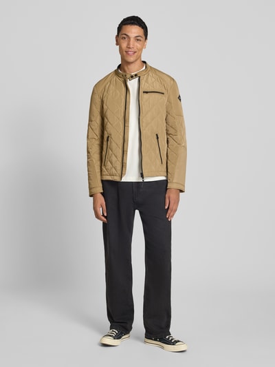 Männermodel trägt Regular Fit Jacke in Stepp-Optik von Replay in Beige, mit Stehkragen und Reißverschlusstaschen, Ganzkörperansicht von vorne. Rückenlänge 65 cm, Schulterbreite 29 cm, Brustweite 38 cm, Ärmellänge 63 cm, Steppstruktur deutlich sichtbar.
