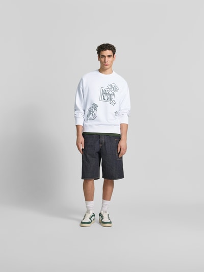 Männermodel trägt Oversized Sweatshirt aus Baumwoll-Mix von MAISON KITSUNÉ mit floralen Label-Stitchings, Weiß und Dunkelblau, Ganzkörperansicht von vorne.