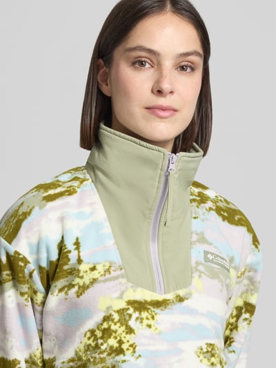 Kobiece model nosi Fleecepullover mit Stehkragen und Reißverschlusstaschen od Columbia, wzór pastelowy, detal z logo, krój regular fit, półzbliżenie na górę ciała