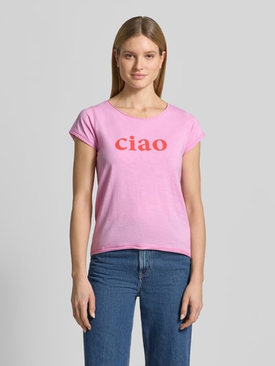 Frauenmodel trägt T-Shirt mit Statement-Print und Rundhalsausschnitt von Christian Berg Woman in Rosa mit rotem Schriftzug, Regular Fit, Baumwolle, Rollsaum, Ganzkörperansicht von vorne.