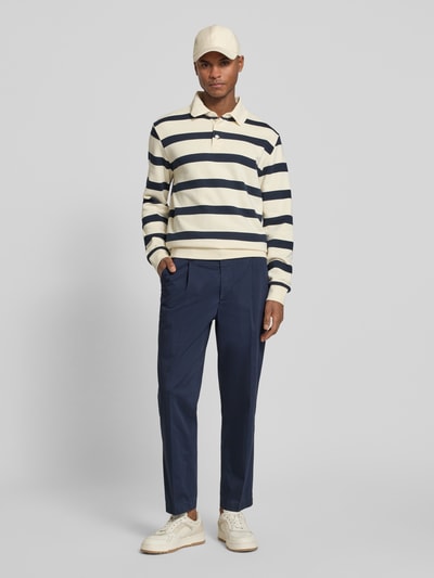 Männermodel trägt Regular Fit Chino aus Baumwoll-Mix Modell 'TAAMIR PLEATED' von Armedangels in Dunkelblau, glatte Struktur, Ganzkörperansicht von vorne.
