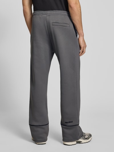 Männermodel trägt Sweatpants mit elastischem Bund und Logo von REVIEW, Relaxed-Fit aus Reine Baumwolle, graue Farbe, Ganzkörperansicht Rückansicht. Innenbeinlänge bei Größe M: 78 cm.
