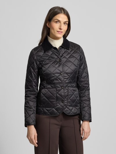Kobiece model nosi kurtkę pikowaną z wykładanym kołnierzem i obszyciem ze sztruksu Deveron od Barbour, taliowany krój, czarny kolor, pikowanie, logo, listwa z zatrzaskami, nakładane kieszenie, lekka watowanie; materiał wytrzymały, widok całej sylwetki z przodu.