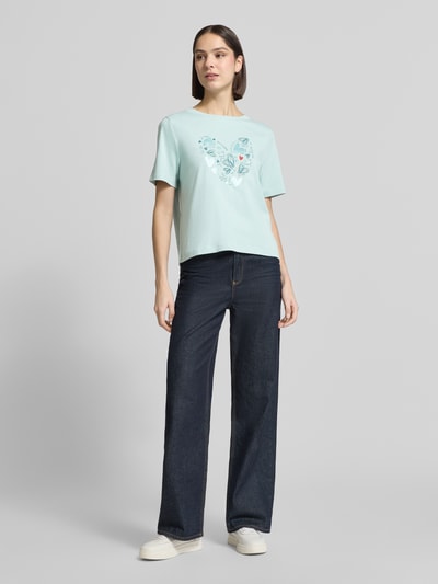Modelka kobieca nosi Relaxed Fit T-Shirt aus reiner Baumwolle od Tom Tailor w jednolitym jasnoniebieskim kolorze z nadrukiem motywu i okrągłym dekoltem, czysta bawełna, krótki rękaw, widok całej sylwetki od przodu.