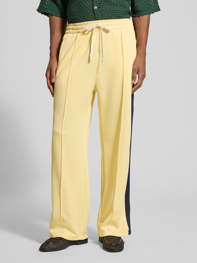 Männermodel trägt Trackpants mit Galonstreifen von ANOTHER COTTON LAB in Gelb mit elastischem Bund und ausgestelltem Bein, Nahaufnahme Unterkörper.