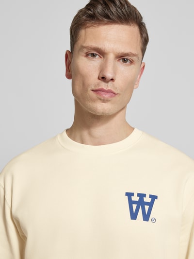 Männermodel trägt Sweatshirt mit Logo-Print Modell 'NOEL' von Wood Wood, aus reiner Baumwolle in Beige, Nahaufnahme Oberkörper.
