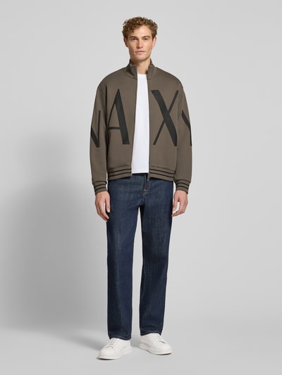 Männermodel trägt Sweatjacke aus Baumwoll-Mix von Armani Exchange in Olive mit großem Label-Print, lockerer Passform, Ganzkörperansicht von vorne.