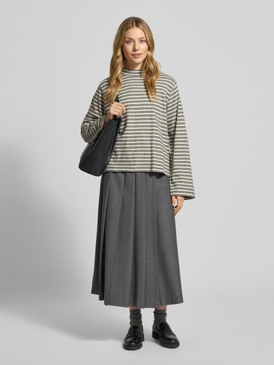 Frauenmodel trägt Regular Fit Langarmshirt aus reiner Baumwolle von Marc O'Polo, Optik: Allover-Muster, gestreift, Rundhals, Ärmelform: langarm, Rumpfabschluss: geschlitzt, Materialverarbeitung: Feinstrick, Farbe beige und grau, kombiniert zu grauem Faltenrock, Ganzkörperansicht von vorne.