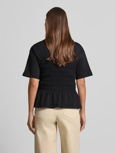 Frauenmodel trägt T-Shirt mit Smok-Details und Rundhalsausschnitt von Jake*s Casual, Reine Baumwolle, Slim-Fit, Rückenlänge 54 cm, schwarze Farbe, glatte und geraffte Textur, Ganzkörperansicht Rückansicht.